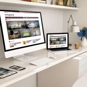 A digital magazine and portfolio website design by AUZ Studio, displayed on an iMac, MacBook, and tablet in a bright office, featuring a grid layout of articles with travel and lifestyle photography.