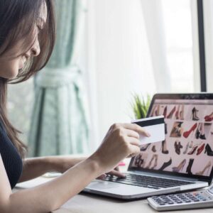A woman smiling while using a credit card to make an online purchase on an e-commerce website designed by AUZ Studio, featuring a responsive grid of fashion footwear.