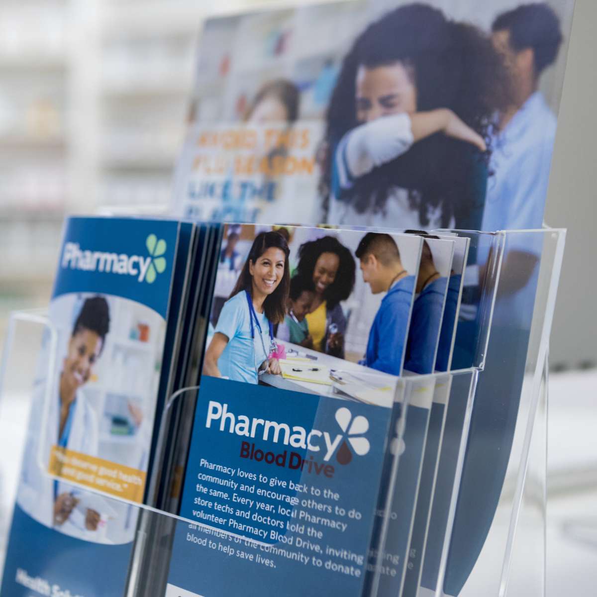 A stack of professional pharmacy blood drive flyers designed by AUZ Studio, displayed in a clear acrylic holder. The flyers feature a blue and white theme with high-quality medical photography and clean typography.