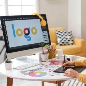 A graphic designer at AUZ Studio using a stylus and drawing tablet to work on a colorful "logo" design on a computer screen in a bright, modern office workspace.