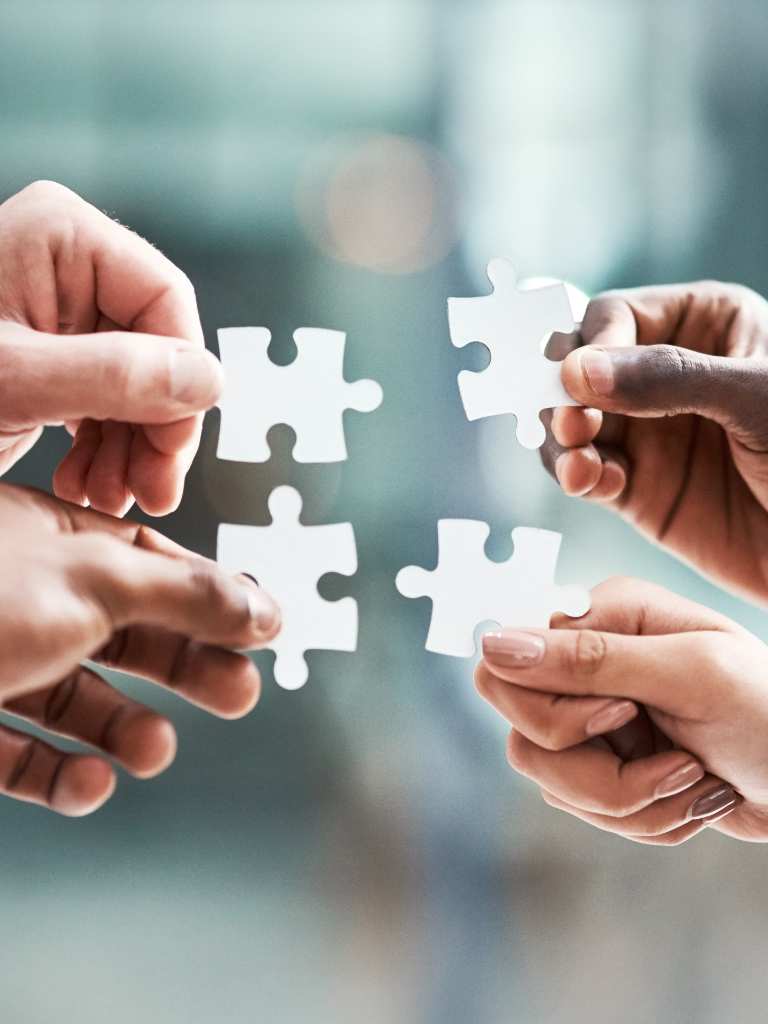 Four hands of diverse individuals coming together to connect four white puzzle pieces, symbolizing the collaborative "Our Story" and core values of AUZ Studio.