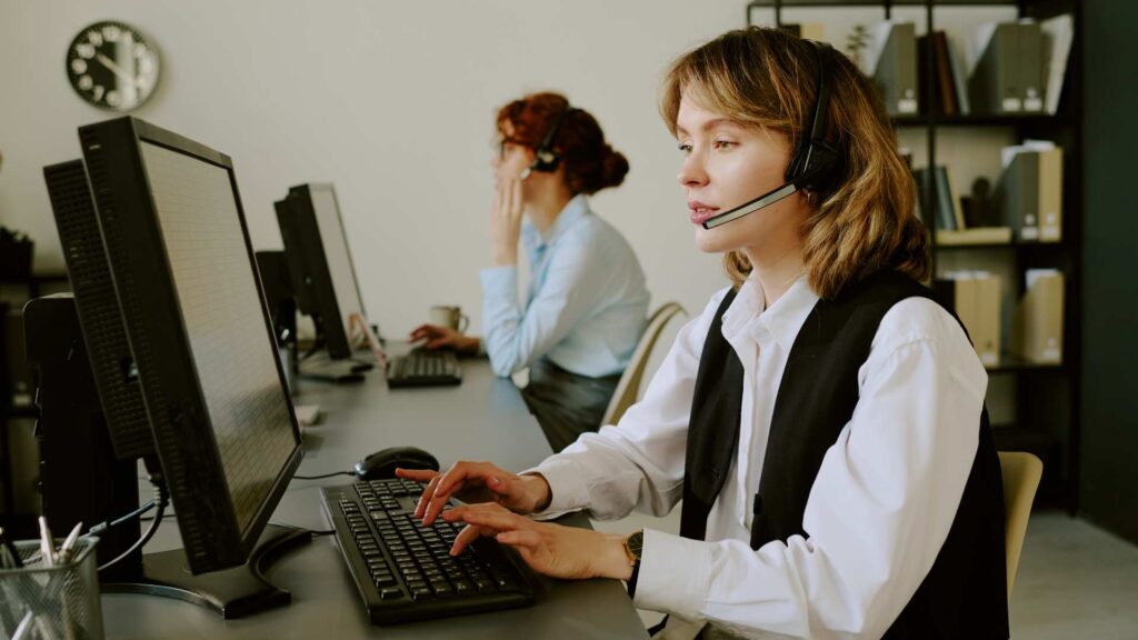 A professional woman wearing a headset and a black vest, typing on a computer keyboard in a bright office while providing premium customer support for AUZ Studio.